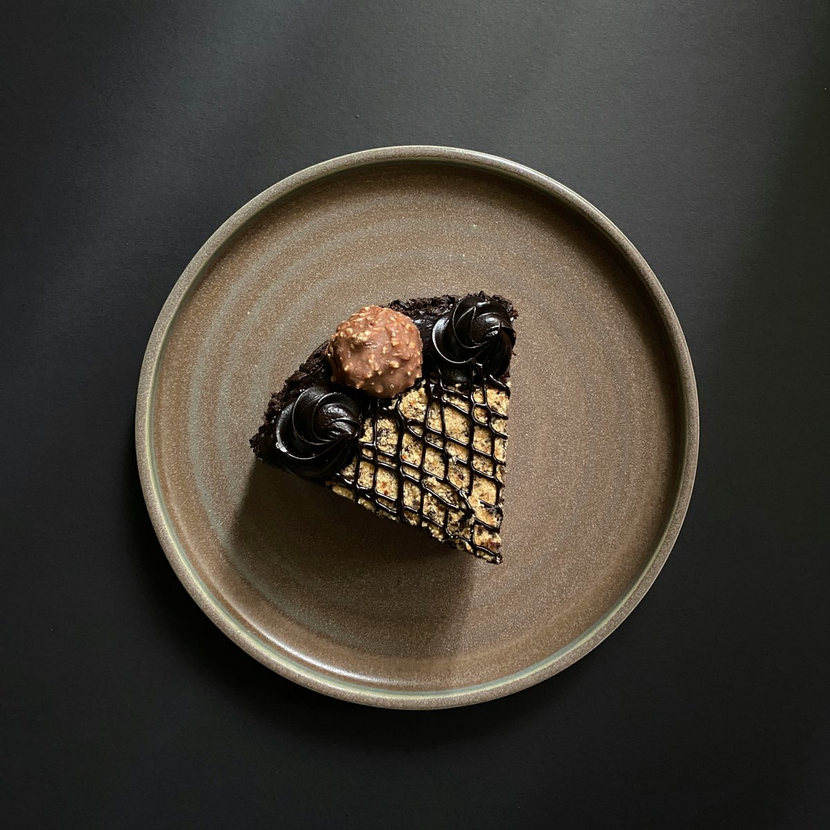 A slice of chocolate hazelnut cake with ganache rosettes and a praline truffle on a stoneware plate, seen from above