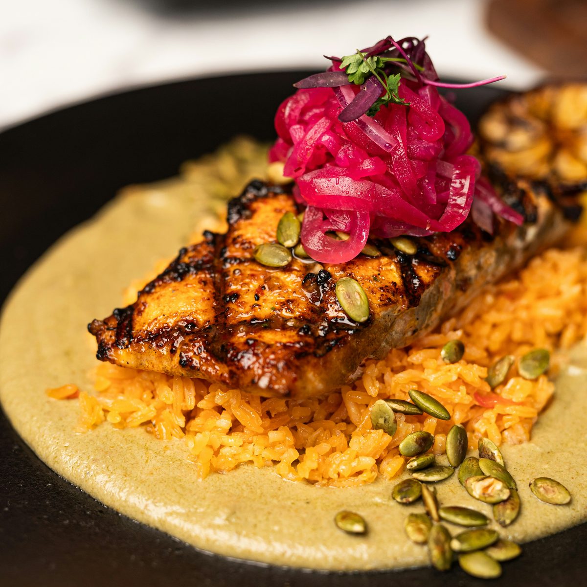 Char-marked glazed salmon on rice and a green herb sauce, topped with pickled red onion and pumpkin seeds